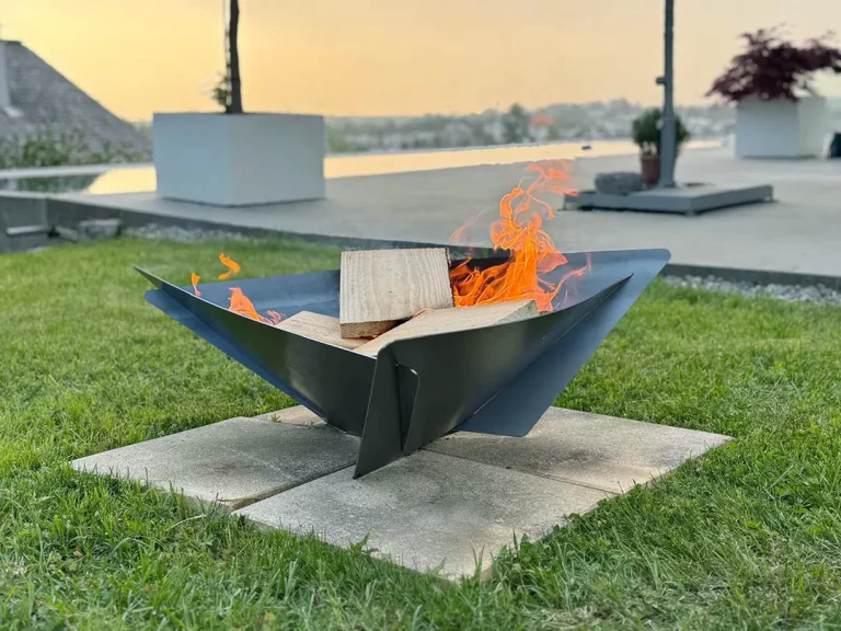 Enara Feuerschale mit Holz und Flammen im Garten neben Terrasse und Pool bei Sonnenuntergang