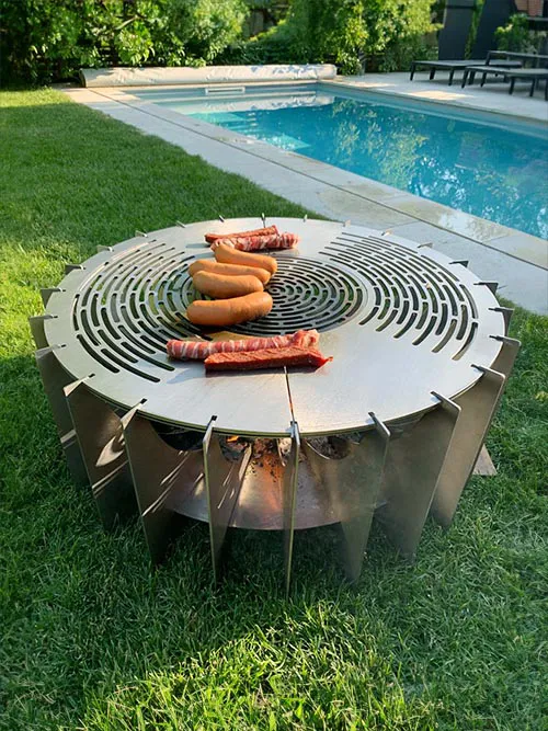 Enara runde Feuerschale im Garten mit Grillplatte und Würstchen